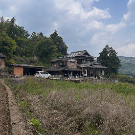 畑の向こうに立つ瓦屋根の古民家